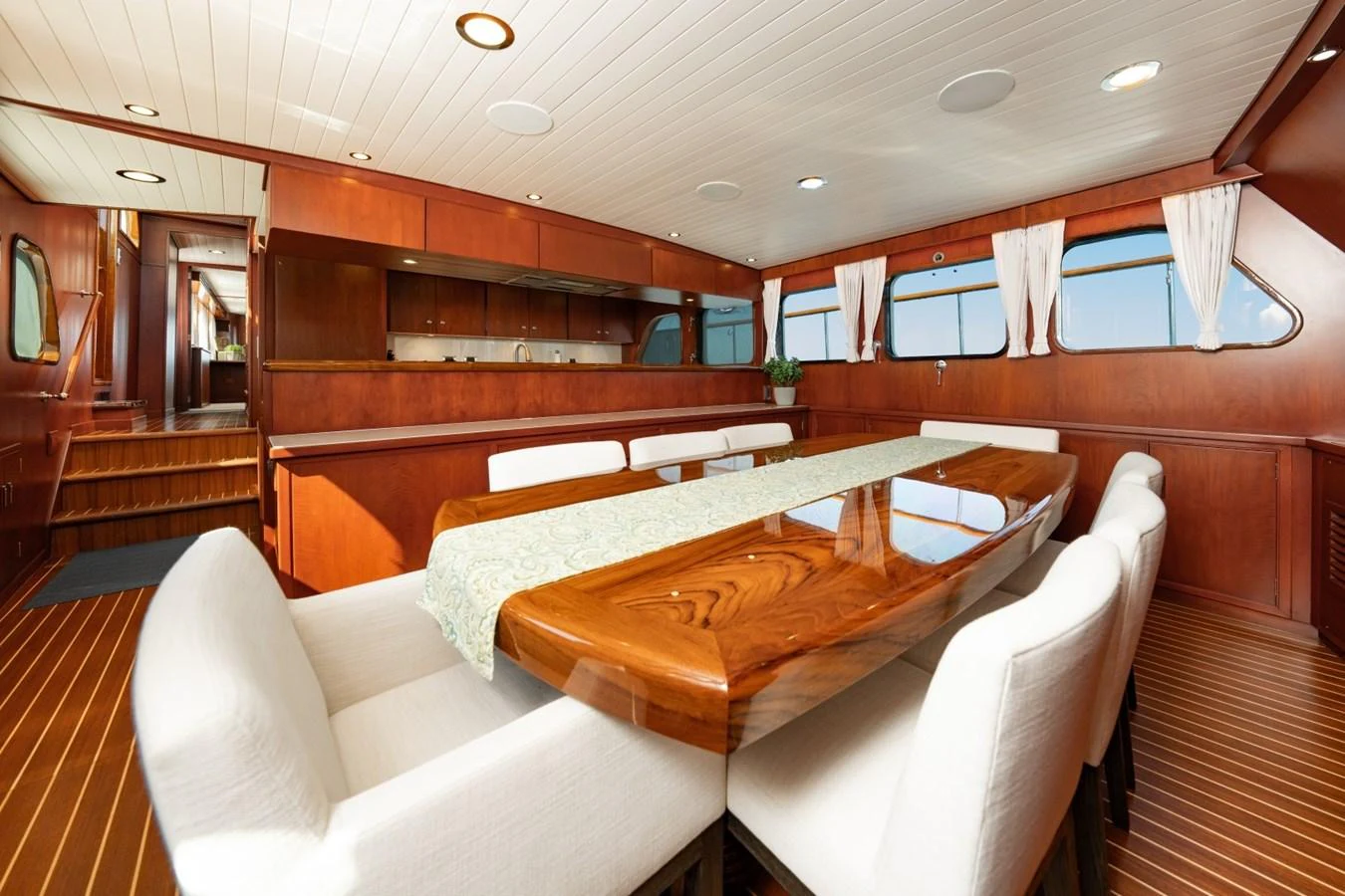 The yacht's dining area features a polished wooden table surrounded by plush white chairs, set against a backdrop of rich wood paneling and large windows. aboard PASSAGE Yacht for Sale