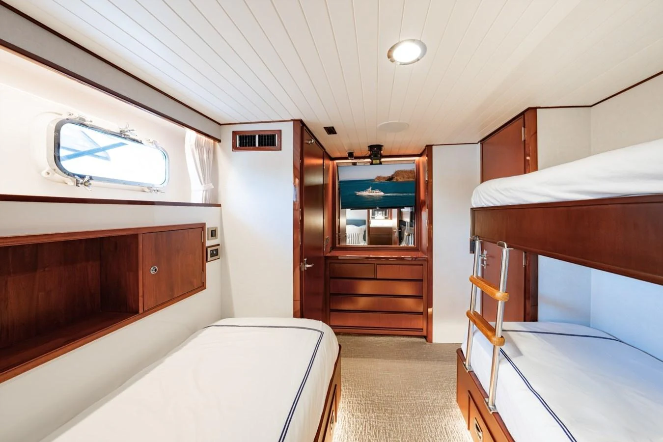 A cozy cabin with twin beds and a bunk bed, featuring warm wooden finishes and a porthole window. aboard PASSAGE Yacht for Sale