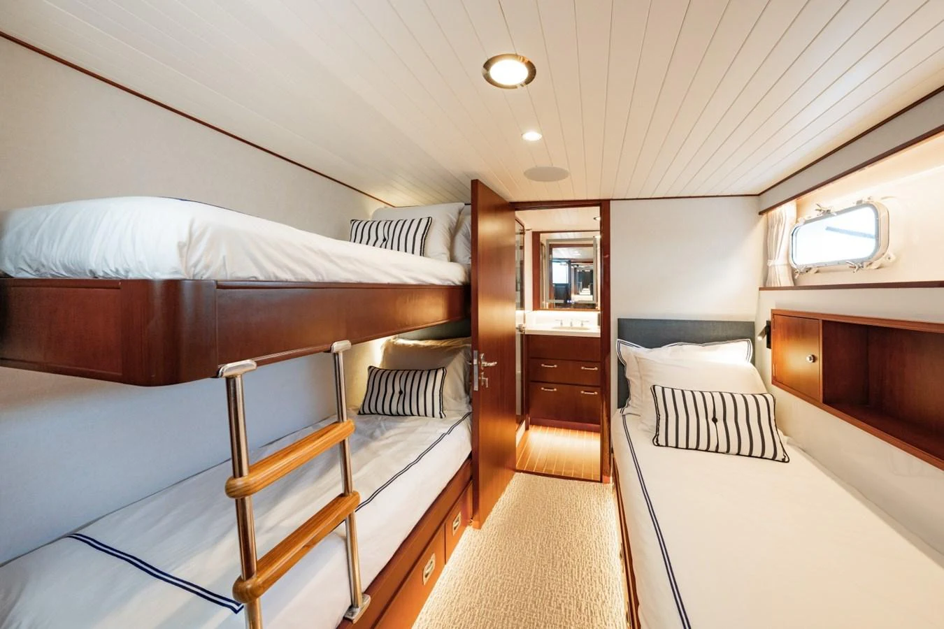 The cozy guest cabin features bunk beds and a single bed with elegant wood finishes and soft lighting. aboard PASSAGE Yacht for Sale