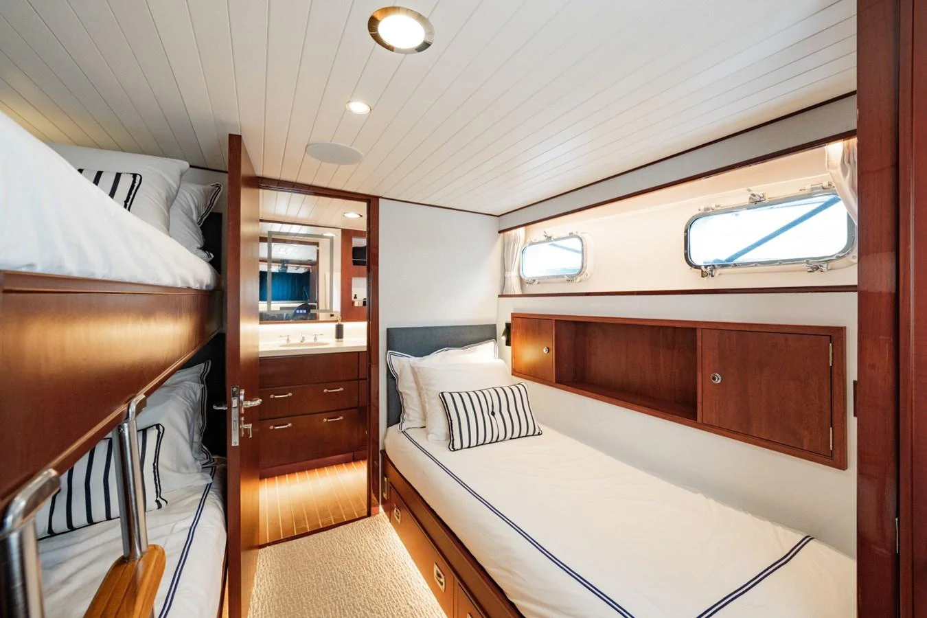 The guest cabin features cozy bunk beds and a single bed with elegant wooden finishes and nautical-themed decor. aboard PASSAGE Yacht for Sale
