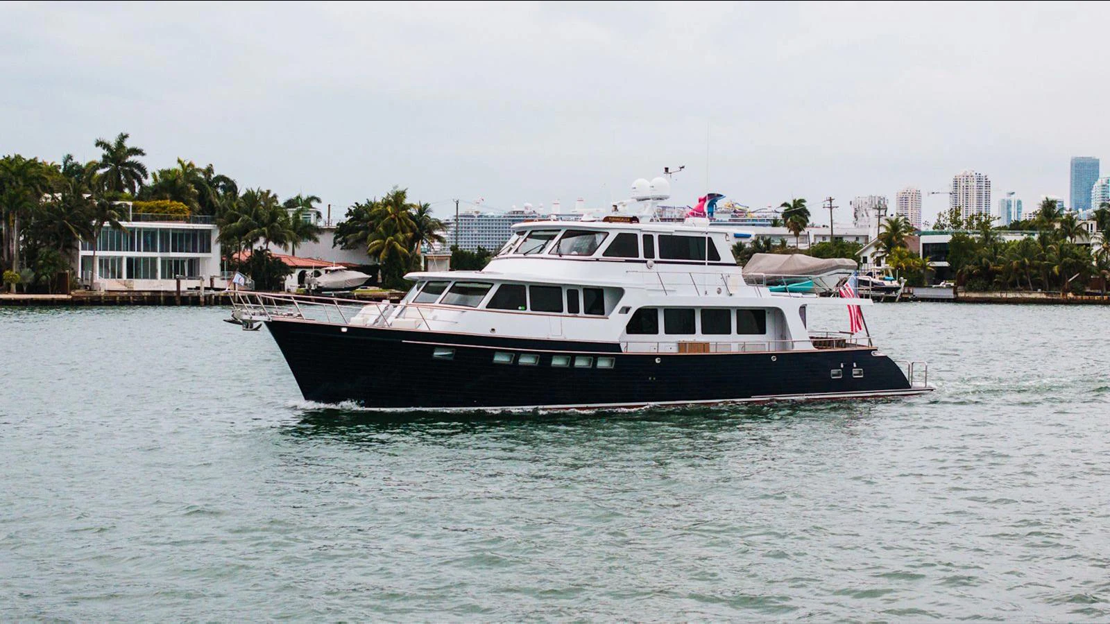 A sleek yacht cruises through calm waters with a cityscape in the background. aboard TURANGALILA Yacht for Sale