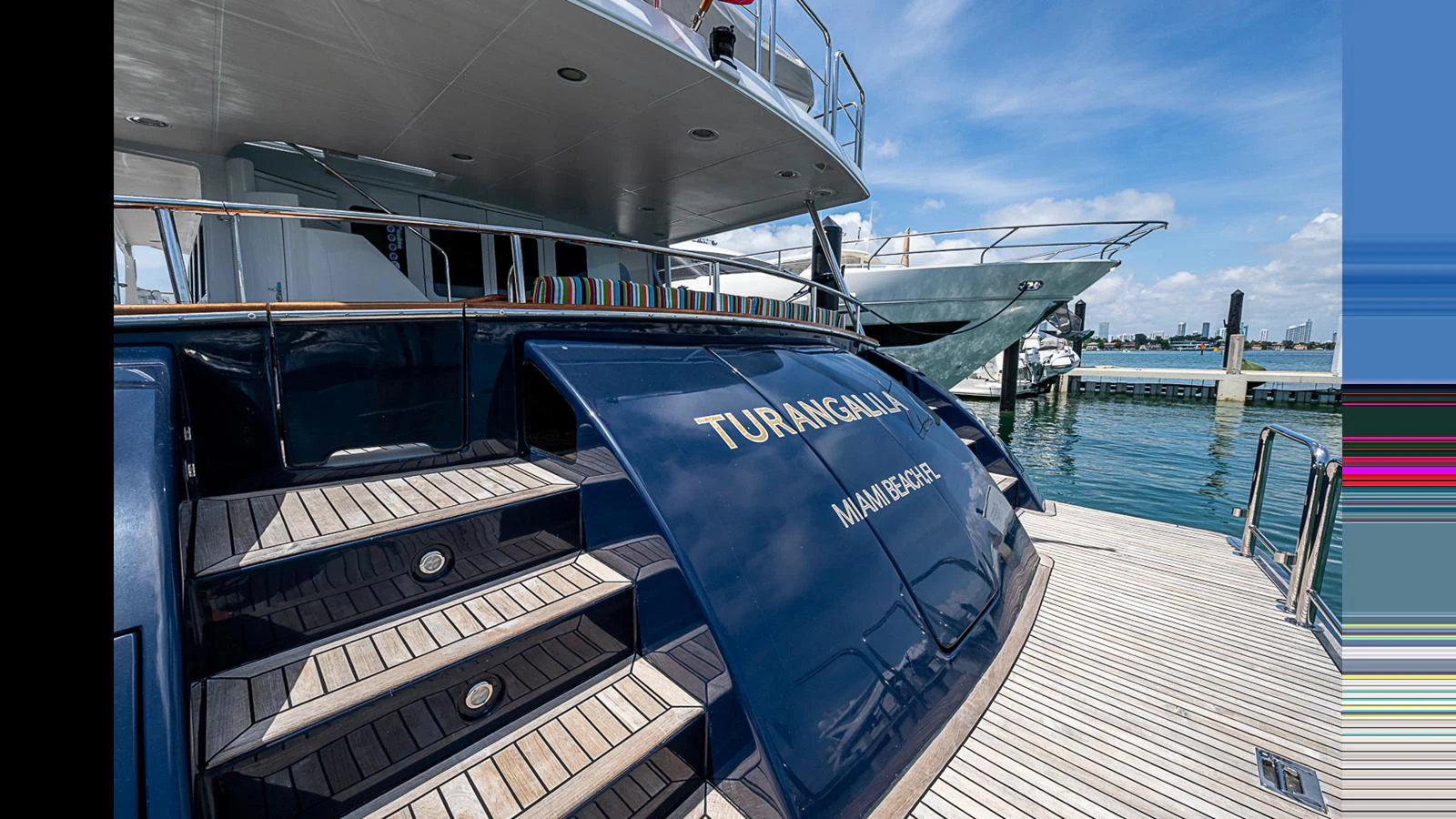 The yacht's aft deck features elegant steps leading up to the main deck, with a polished finish and a view of the marina. aboard TURANGALILA Yacht for Sale