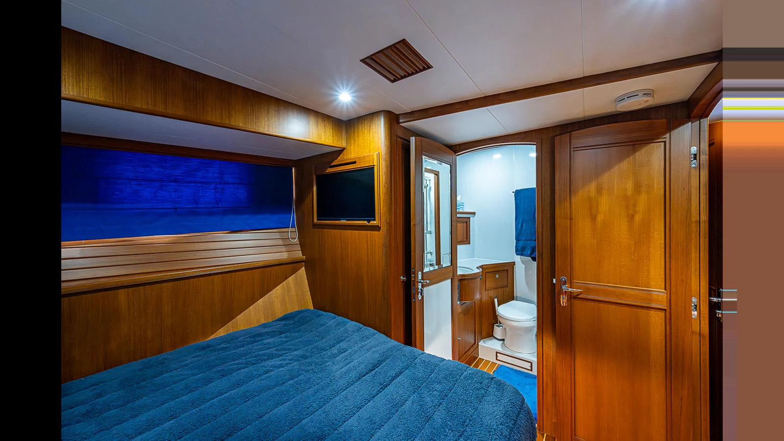 The stateroom features warm wood paneling and a cozy bed, leading to an en-suite bathroom. aboard TURANGALILA Yacht for Sale