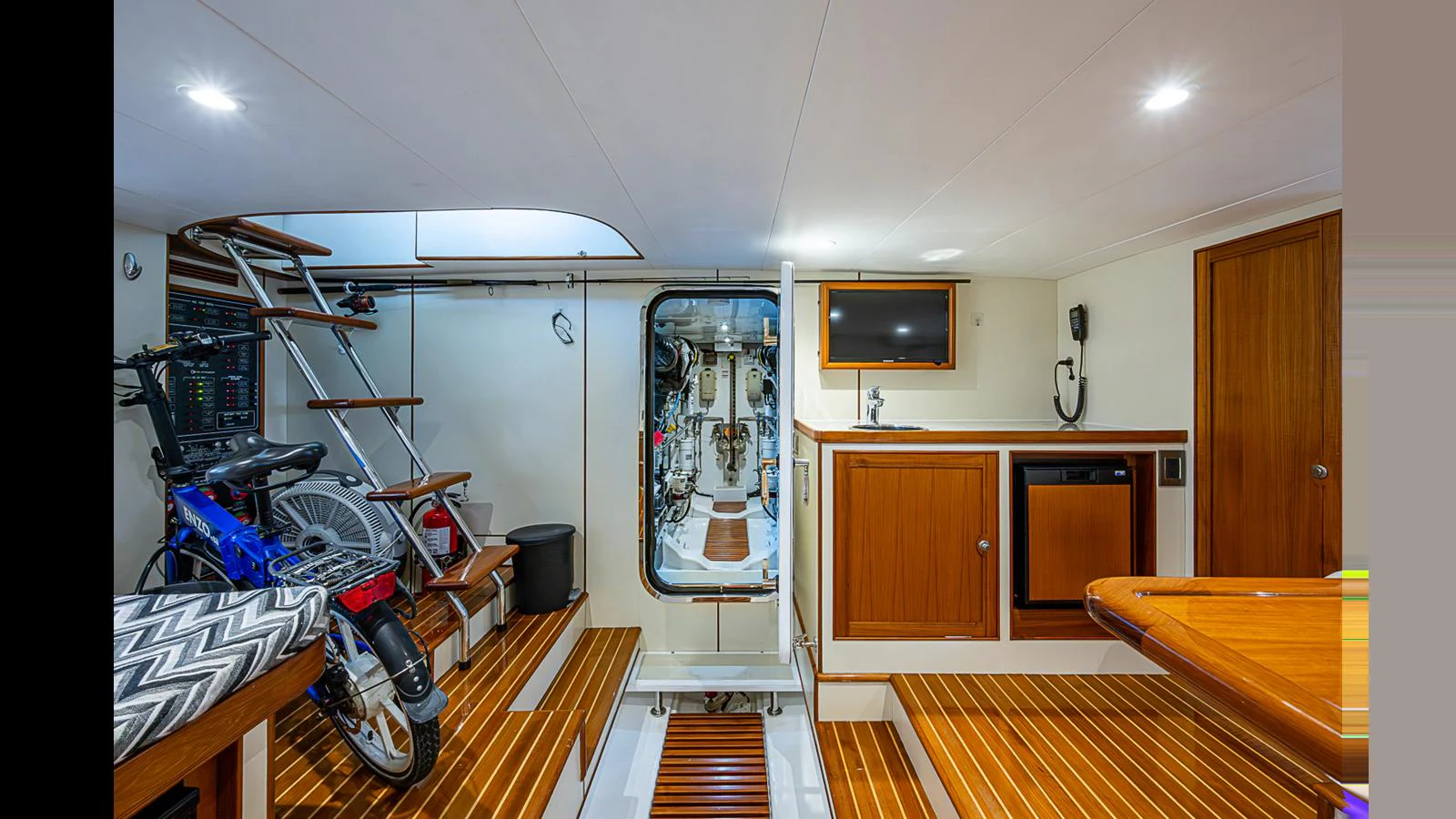 The interior features a well-organized space with wooden flooring, a bicycle, and access to the engine room. aboard TURANGALILA Yacht for Sale