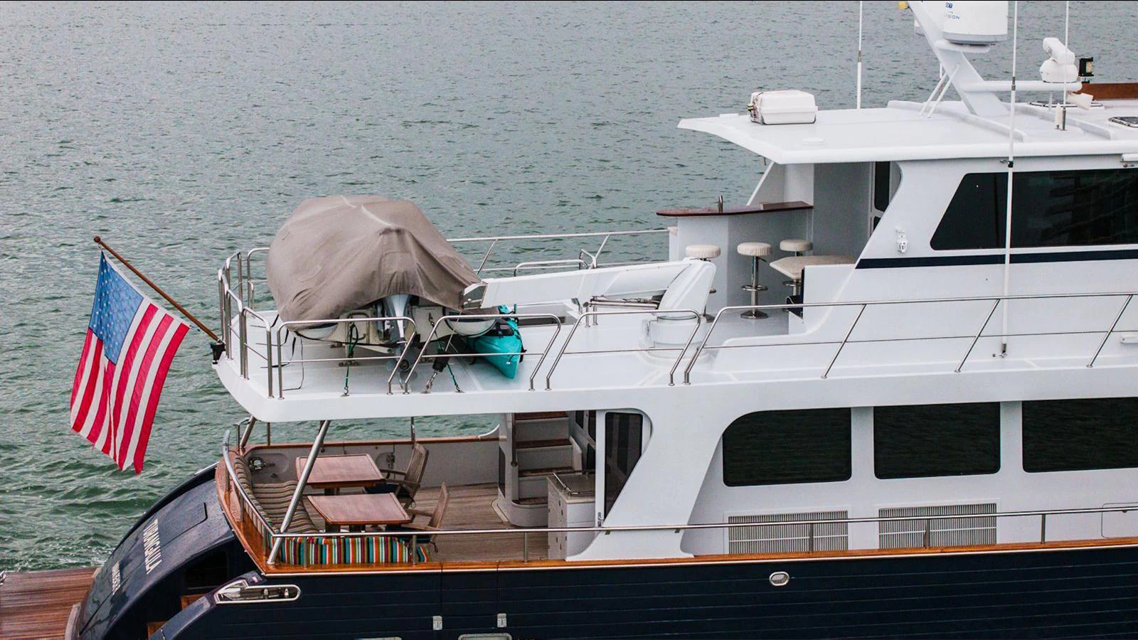 The yacht's aft deck features a covered seating area and an American flag, with the vessel docked by the water. aboard TURANGALILA Yacht for Sale