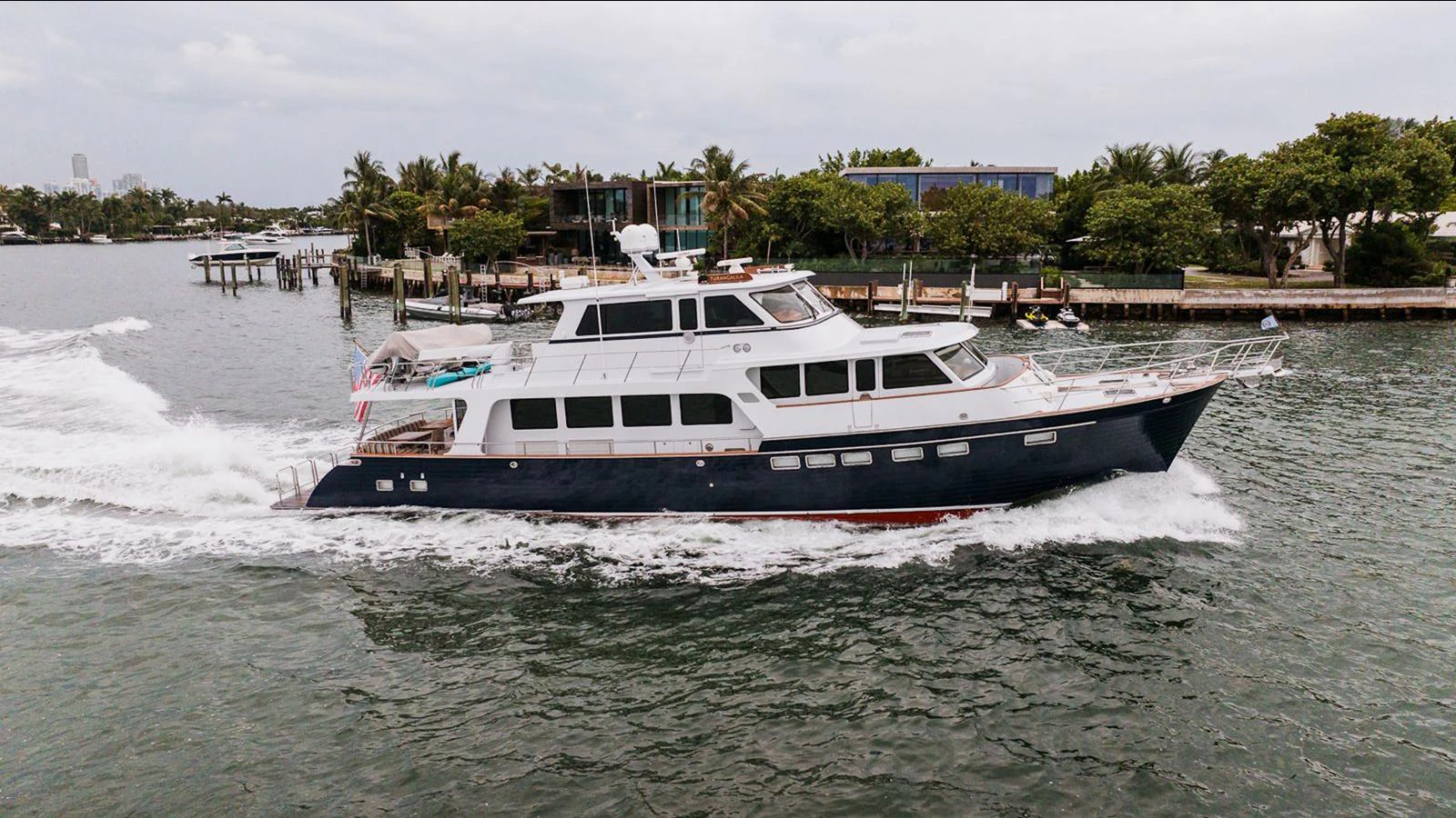 A sleek yacht cruises through calm waters near a coastal area with lush greenery. aboard TURANGALILA Yacht for Sale