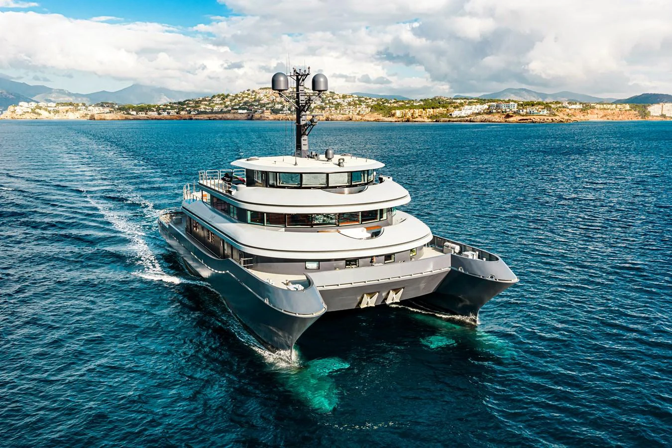 A luxurious yacht cruises through pristine blue waters with a scenic coastline in the background. aboard NURJA Yacht for Sale