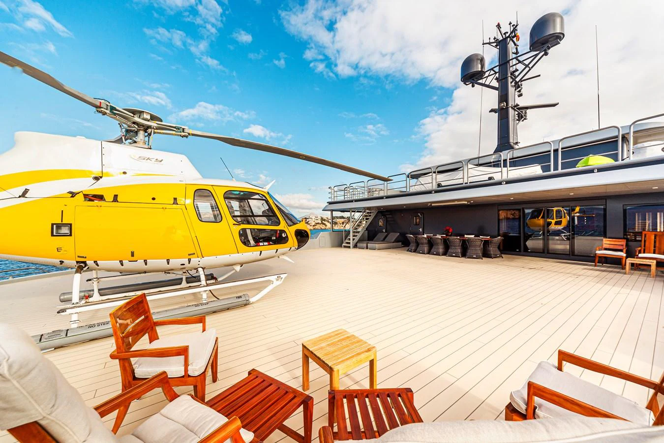 The yacht features a spacious helipad with a helicopter and comfortable seating area under a clear sky. aboard NURJA Yacht for Sale