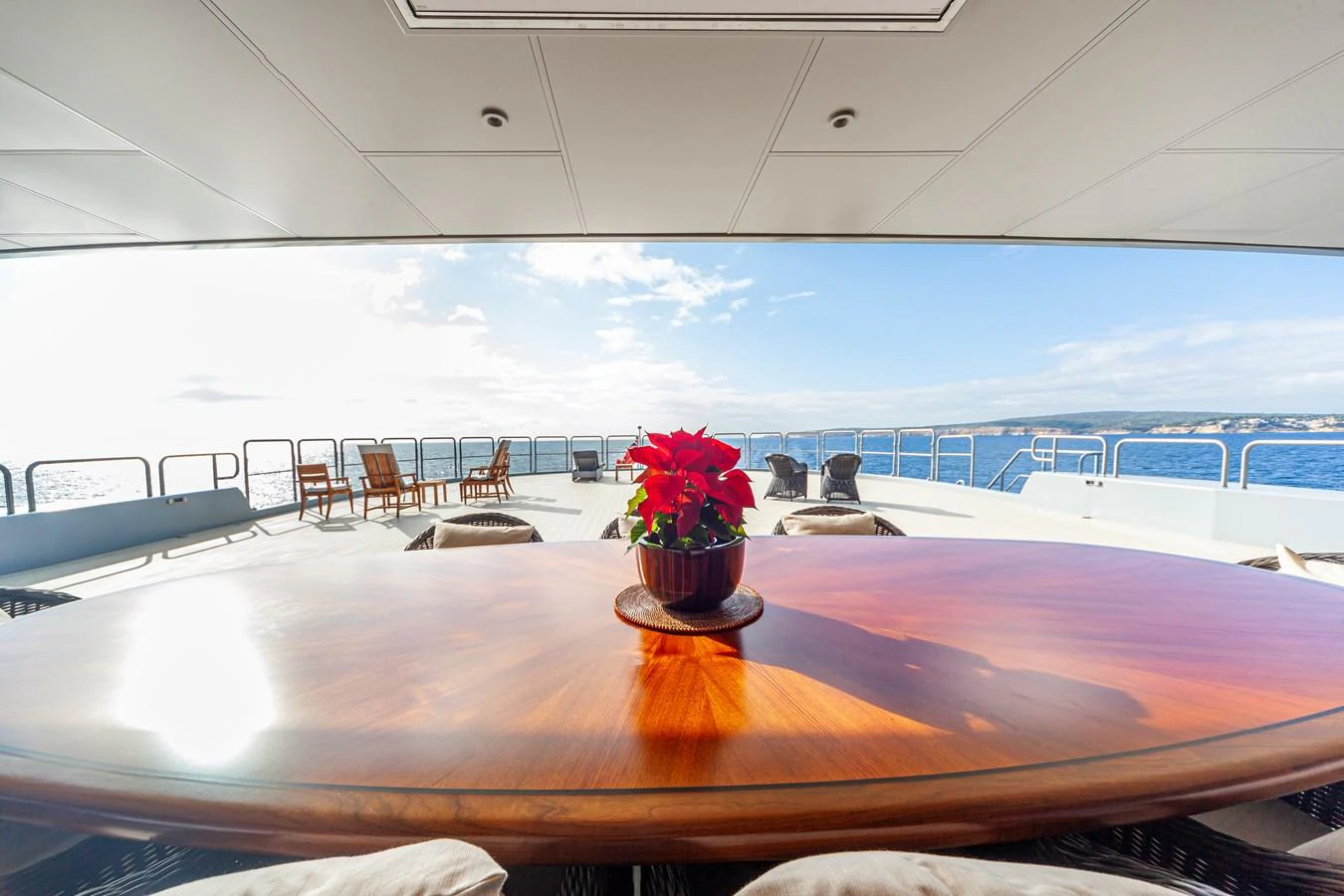 The aft deck features a polished wooden table with a vibrant red poinsettia centerpiece, offering a serene ocean view. aboard NURJA Yacht for Sale