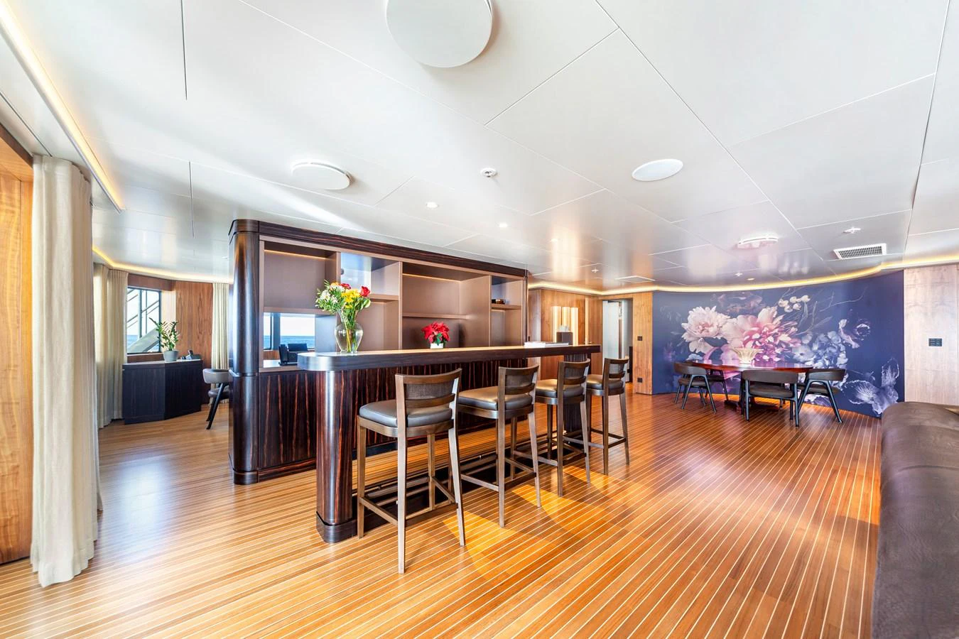 The spacious salon features elegant wood flooring, a stylish bar area, and a large mural, creating a luxurious and inviting atmosphere. aboard NURJA Yacht for Sale