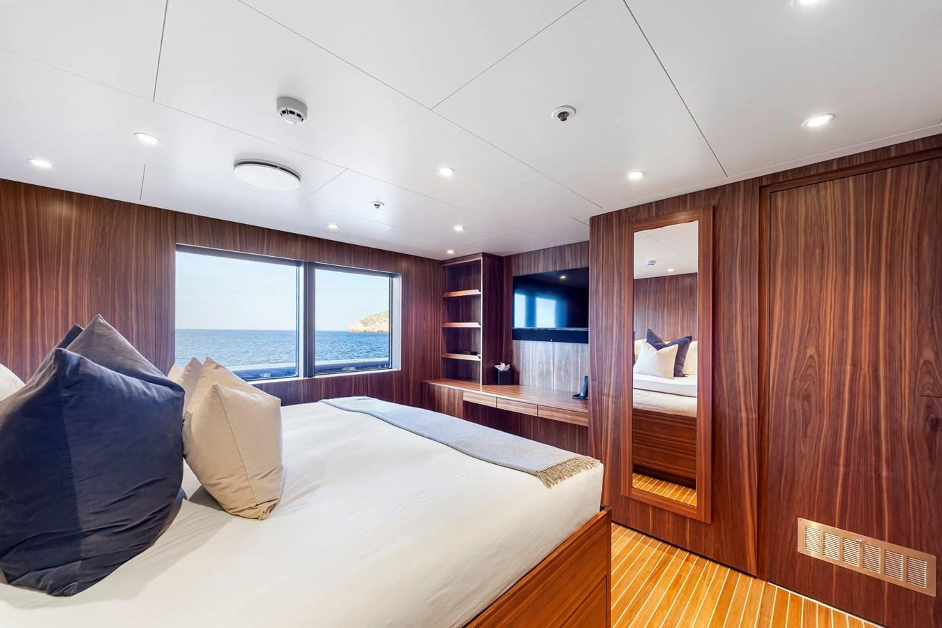 A luxurious stateroom with a large bed, wood paneling, and a scenic ocean view. aboard NURJA Yacht for Sale