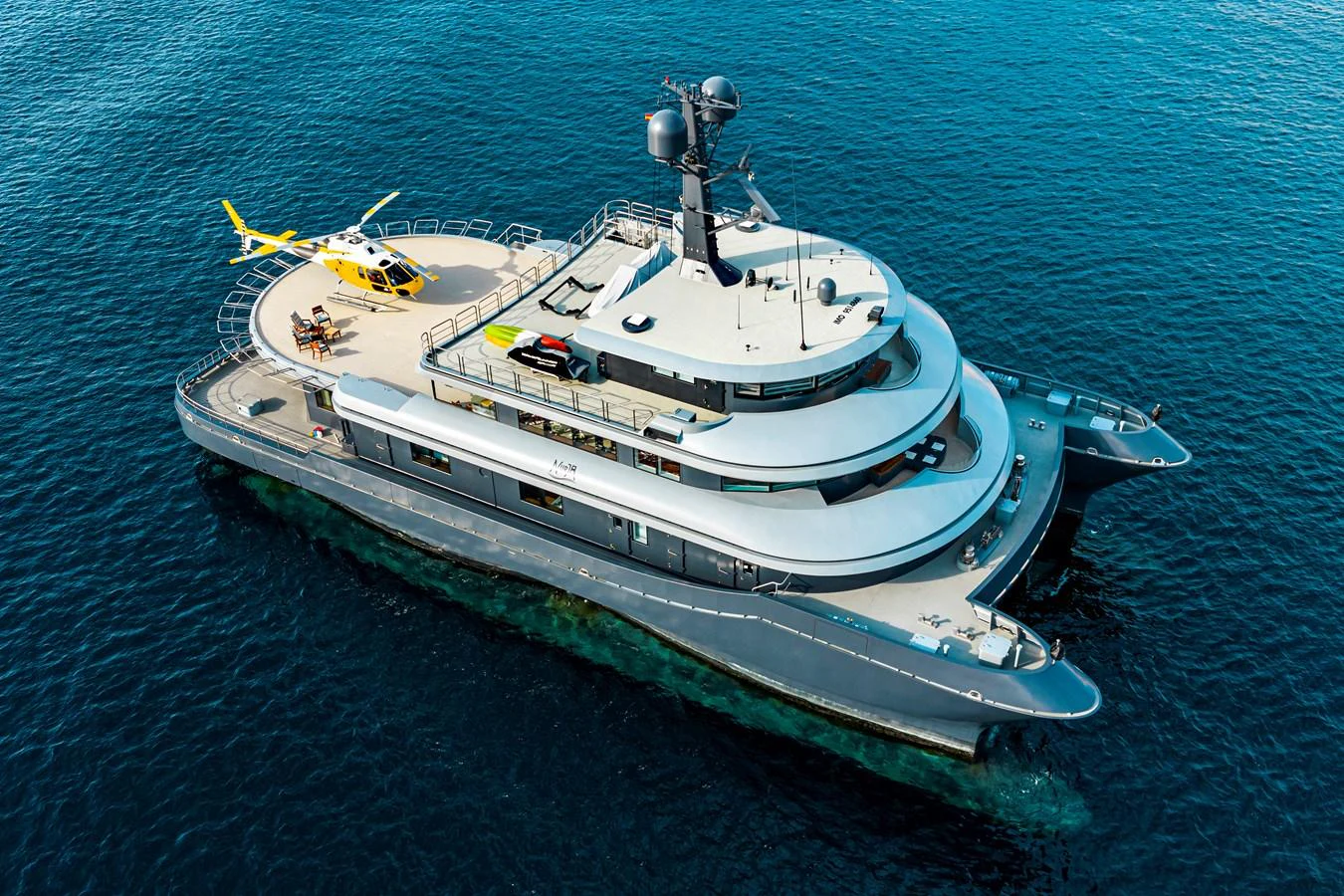 This striking yacht features a spacious deck with a helicopter landing pad, cruising elegantly on the open water. aboard NURJA Yacht for Sale