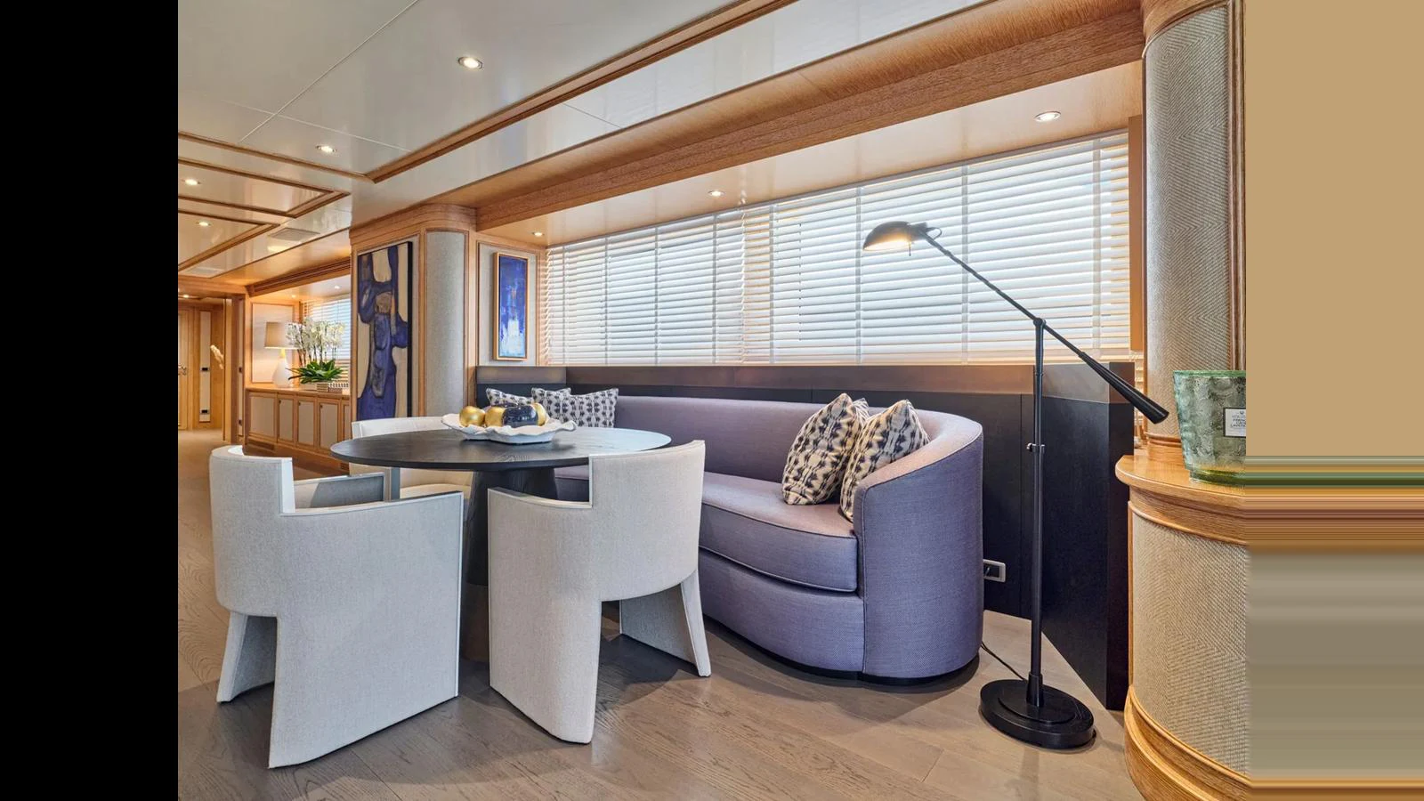 The yacht's salon features a cozy seating area with a round dining table and modern chairs, complemented by a stylish floor lamp and large windows. aboard THEOLINA Yacht for Sale