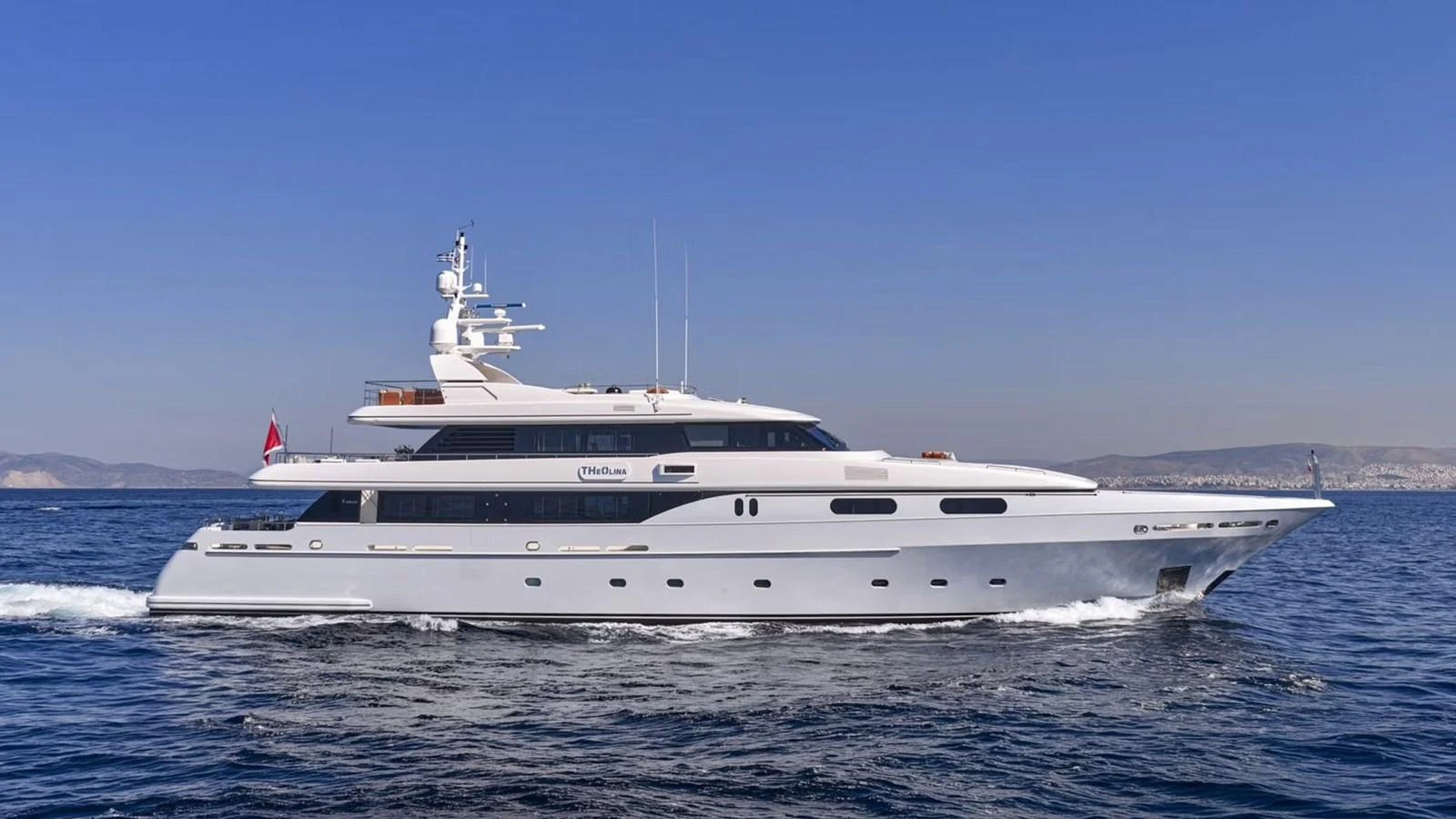 A sleek and elegant yacht cruising on calm waters under a clear blue sky. aboard THEOLINA Yacht for Sale