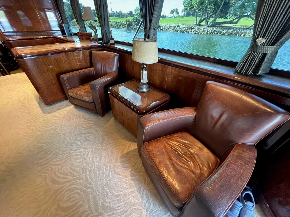 The yacht's interior features a cozy seating area with leather chairs and a view of the water through large windows. aboard WISH YOU WERE HERE Yacht for Sale