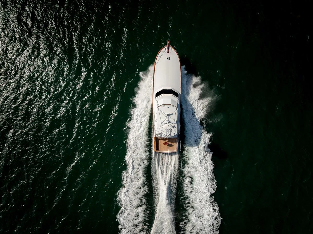 Aerial view of a sleek yacht cruising through the water, leaving a trail of white wake behind. aboard WISH YOU WERE HERE Yacht for Sale
