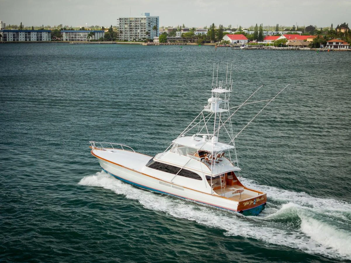 A sleek yacht cruises through calm waters with a cityscape in the background. aboard WISH YOU WERE HERE Yacht for Sale