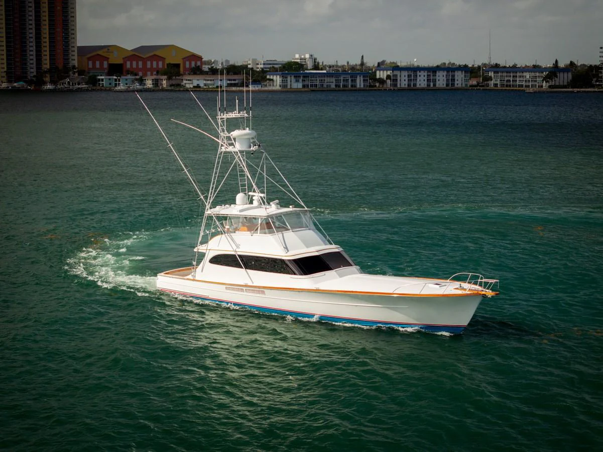 A sleek sportfishing yacht cruises through calm waters with a cityscape in the background. aboard WISH YOU WERE HERE Yacht for Sale