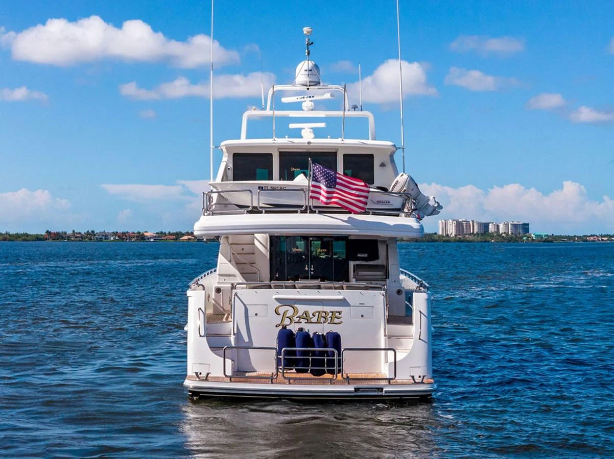A luxurious yacht is shown from the rear, cruising on calm waters under a clear blue sky. aboard BABE Yacht for Sale