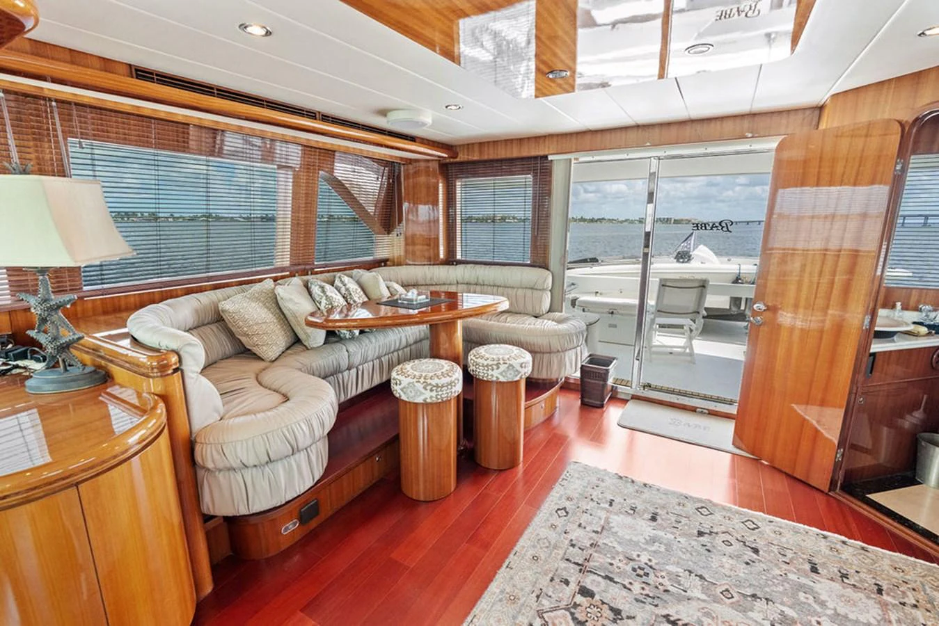 The salon features plush seating, a wooden dining table, and large windows offering a view of the water. aboard BABE Yacht for Sale