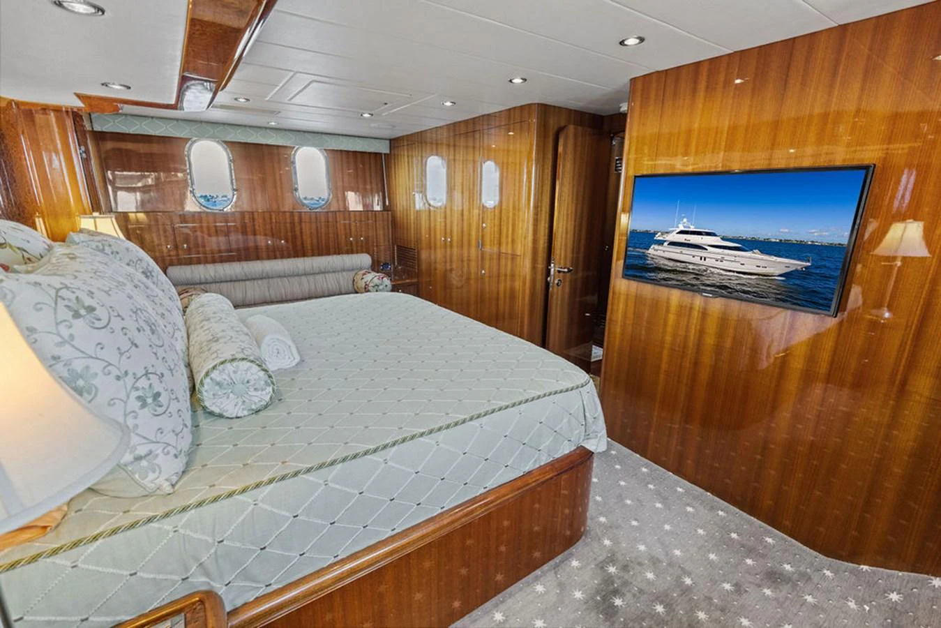 The master stateroom features a luxurious bed, elegant wood paneling, and a flat-screen TV displaying a yacht. aboard BABE Yacht for Sale