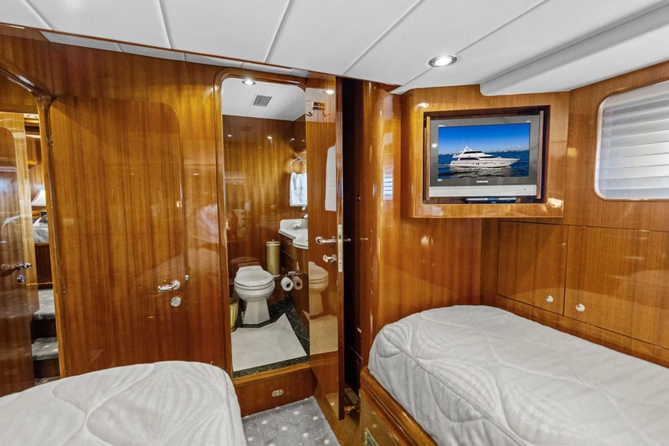 The guest stateroom features twin beds, a flat-screen TV, and an ensuite bathroom with elegant wood finishes. aboard BABE Yacht for Sale