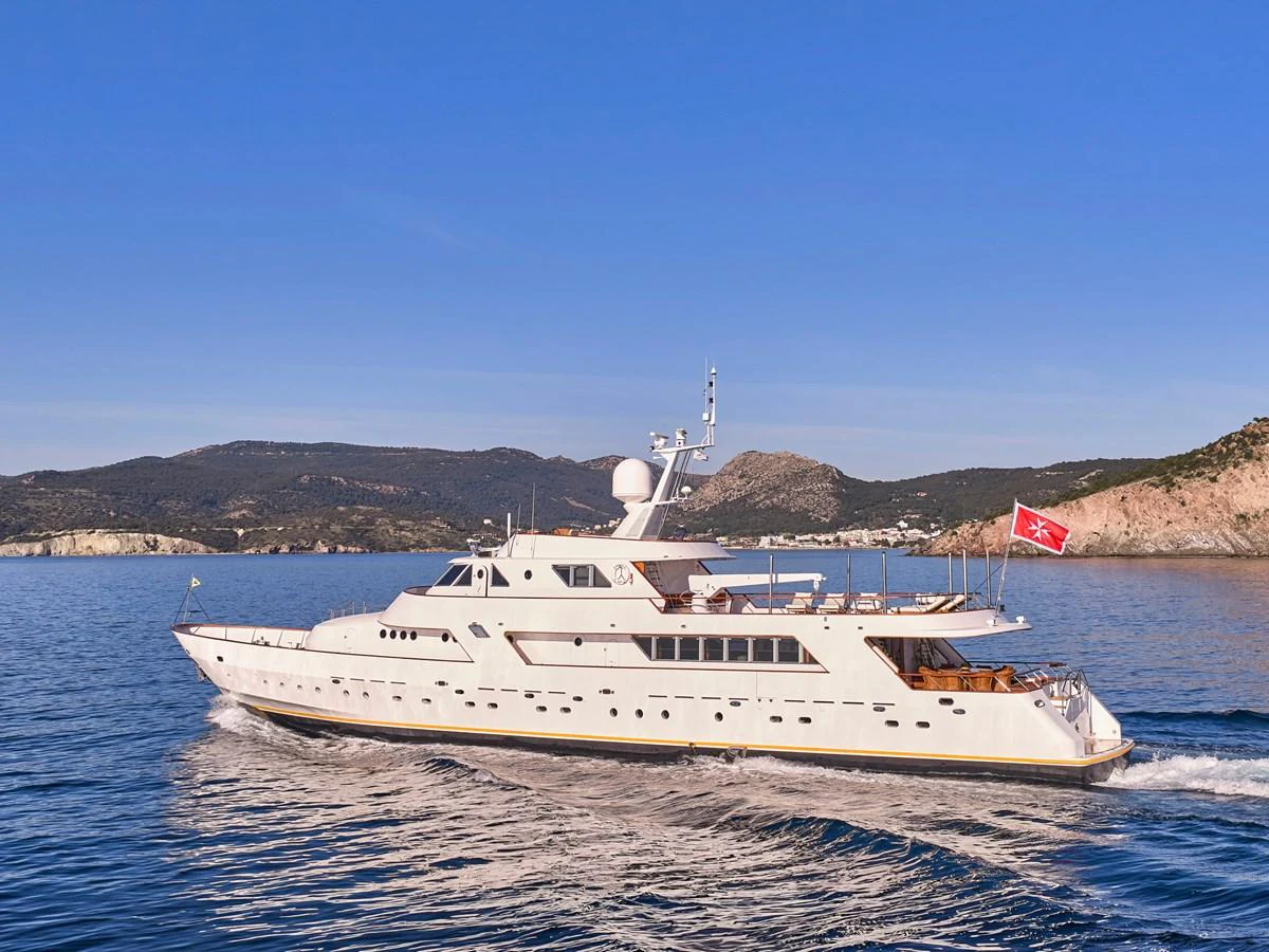 A classic yacht cruises gracefully on calm waters with scenic hills in the background. aboard RESINA Yacht for Sale