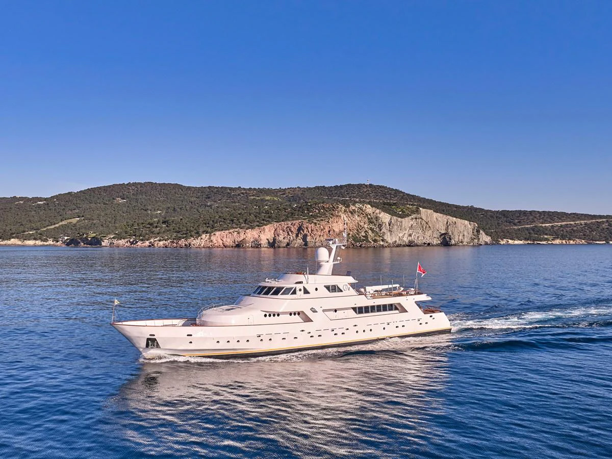 A luxurious yacht cruises through calm waters with a scenic coastline in the background. aboard RESINA Yacht for Sale