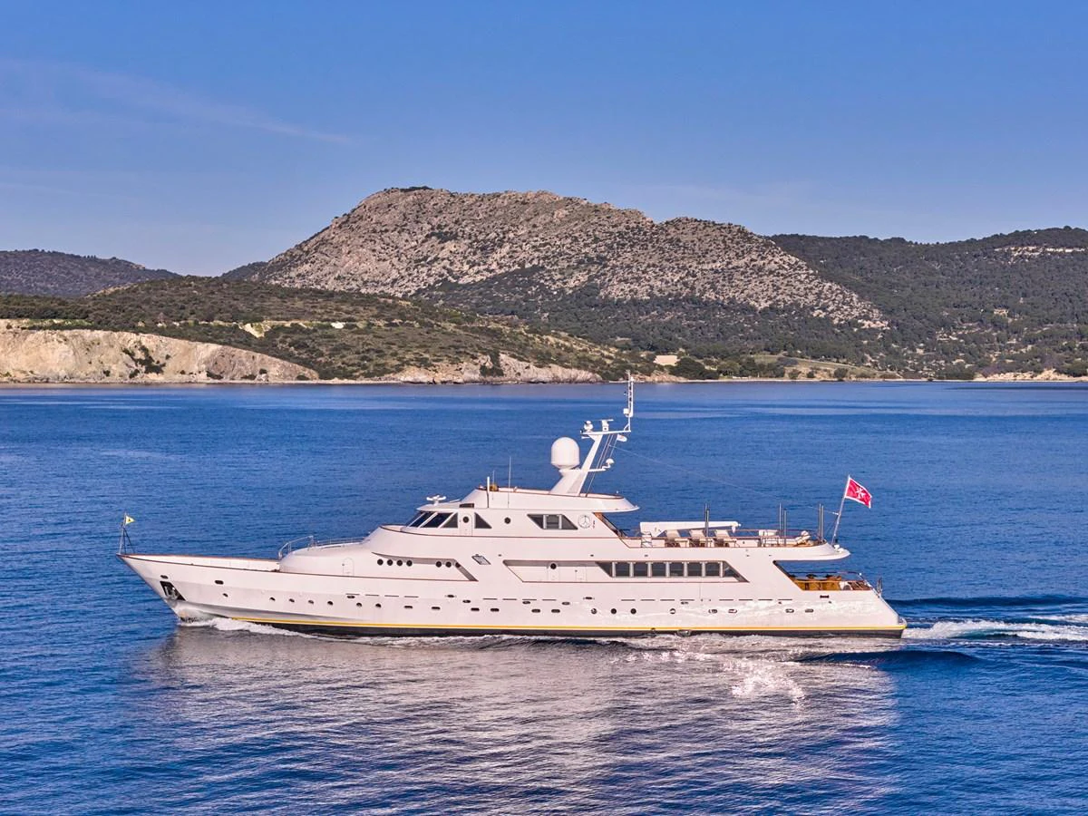 A stunning yacht cruises gracefully on calm waters with scenic hills in the background. aboard RESINA Yacht for Sale