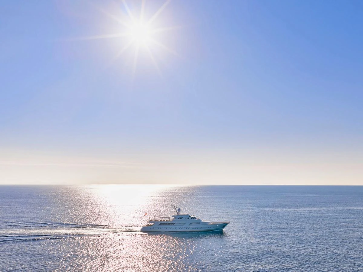 A sleek yacht cruises under a bright sun on calm, open waters. aboard RESINA Yacht for Sale