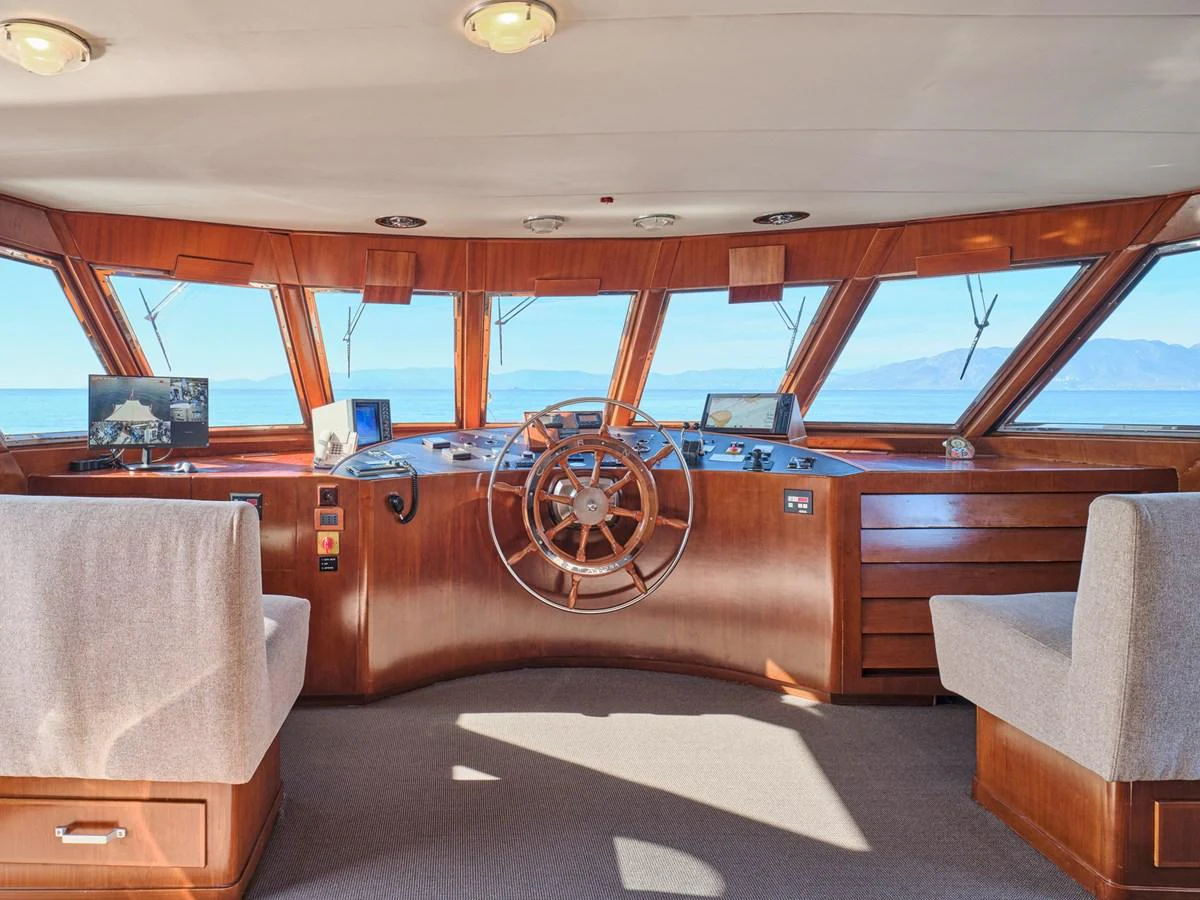 The yacht's helm features a classic wooden steering wheel and panoramic windows offering stunning ocean views. aboard RESINA Yacht for Sale
