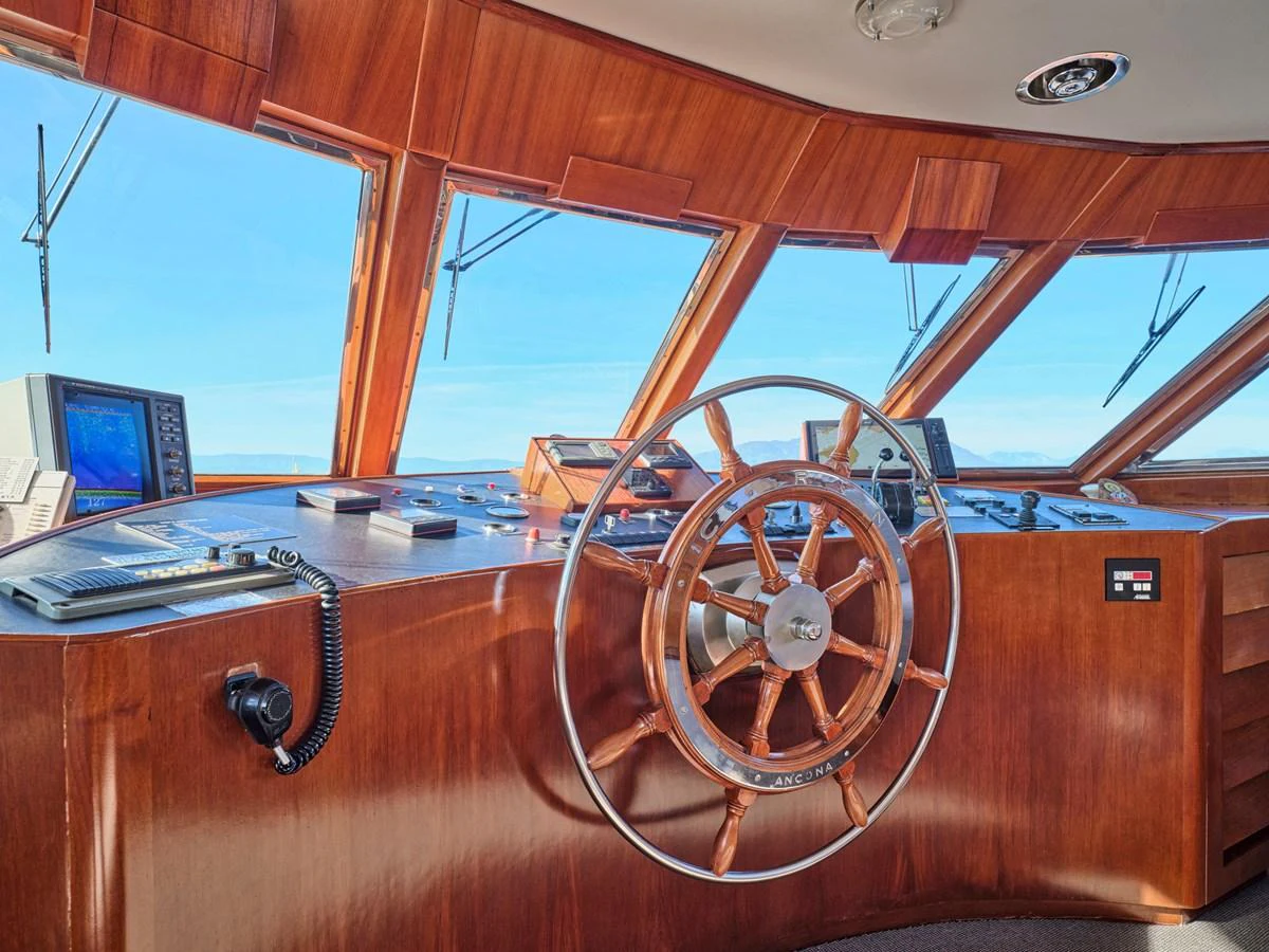 The helm station features a classic wooden steering wheel and modern navigation equipment, offering a blend of tradition and technology. aboard RESINA Yacht for Sale