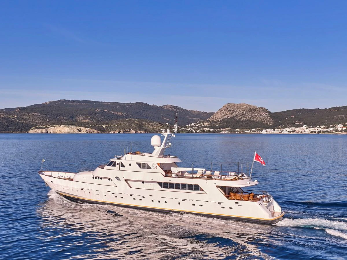 A stunning yacht glides through calm waters with a picturesque coastal backdrop. aboard RESINA Yacht for Sale