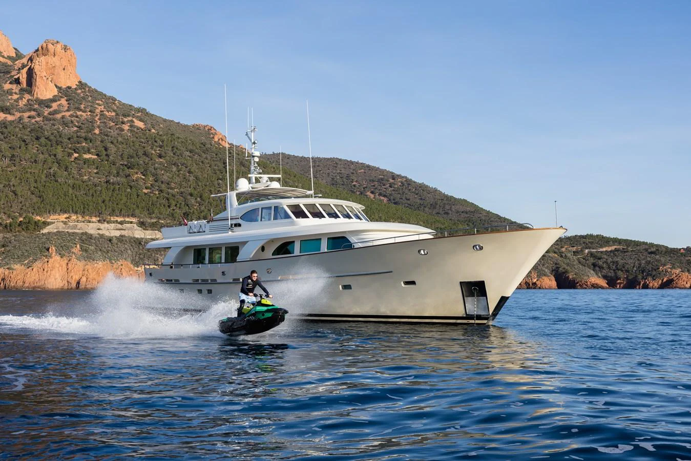 A sleek yacht cruises along the coastline with a jet ski speeding nearby. aboard ORIZZONTE Yacht for Sale