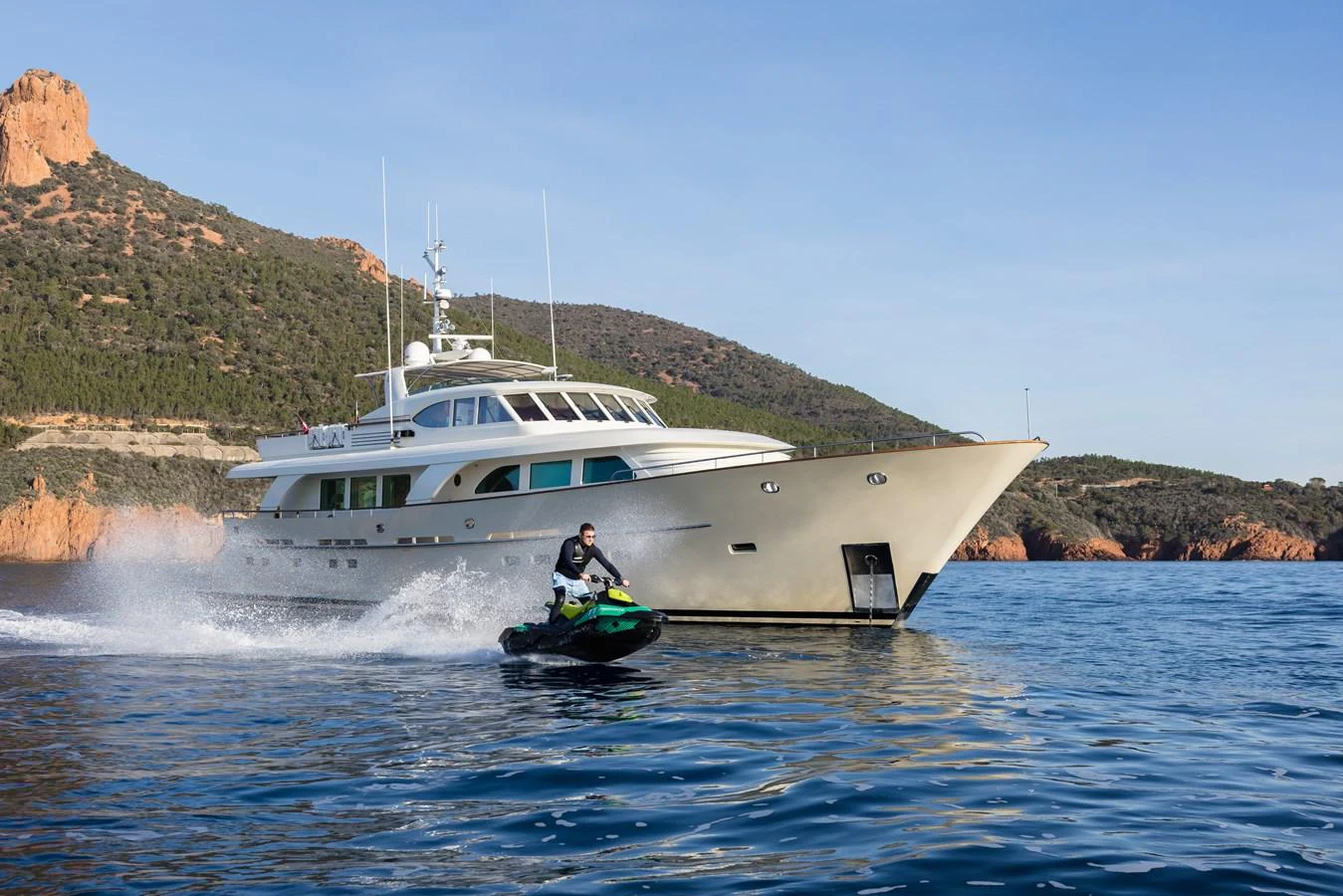 A sleek yacht cruises through serene waters with a jet ski rider in the foreground. aboard ORIZZONTE Yacht for Sale