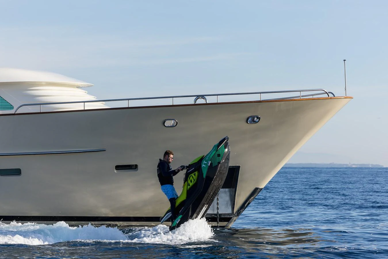 A sleek yacht cruises on the water as a person rides a jet ski nearby. aboard ORIZZONTE Yacht for Sale
