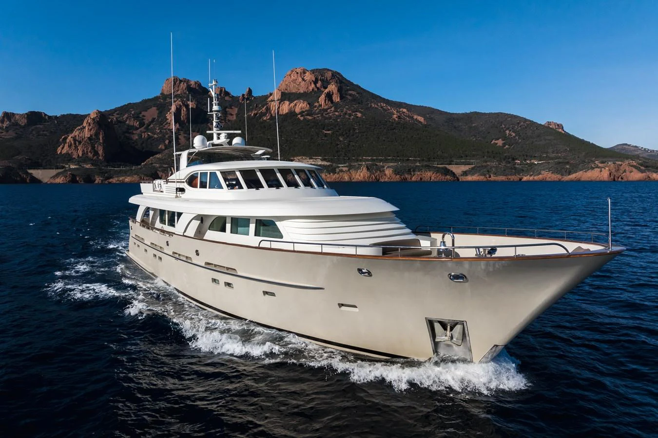 A sleek yacht cruises through the water with a scenic mountainous backdrop. aboard ORIZZONTE Yacht for Sale