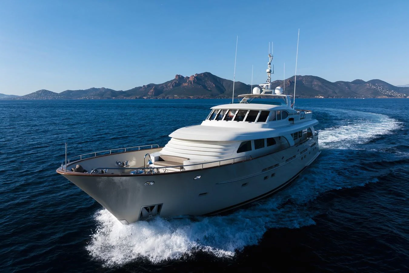 A sleek yacht cruises through calm waters with a mountainous backdrop. aboard ORIZZONTE Yacht for Sale