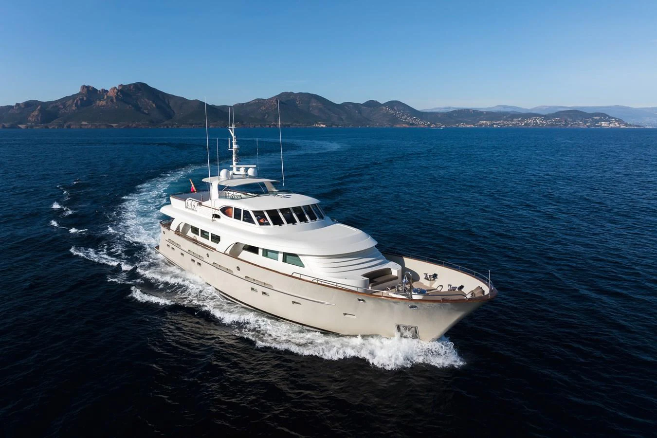 A luxurious yacht cruises through clear blue waters with a stunning mountainous backdrop. aboard ORIZZONTE Yacht for Sale