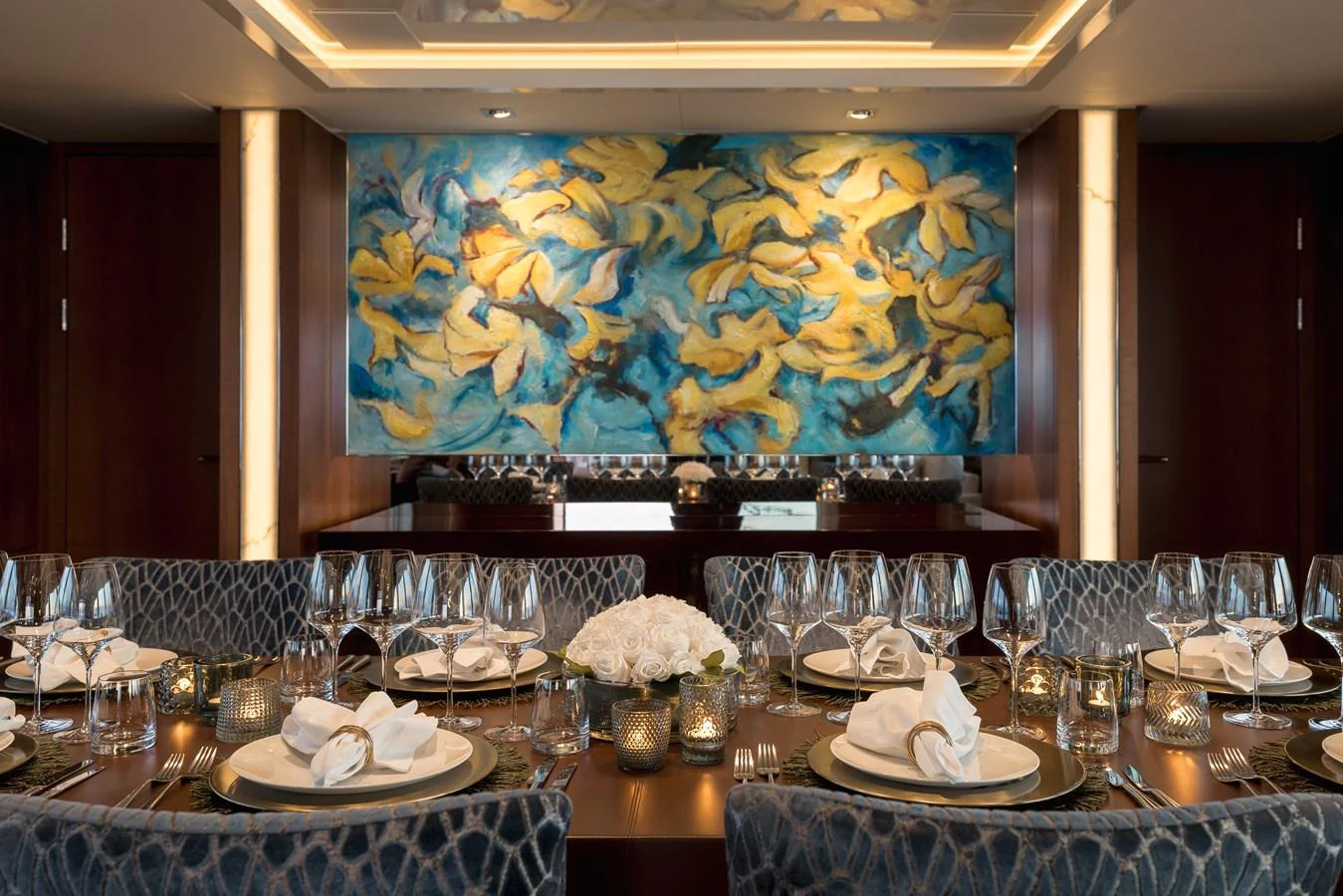 The yacht's dining area features an elegant table setting with a vibrant, artistic backdrop. aboard ORIZZONTE Yacht for Sale