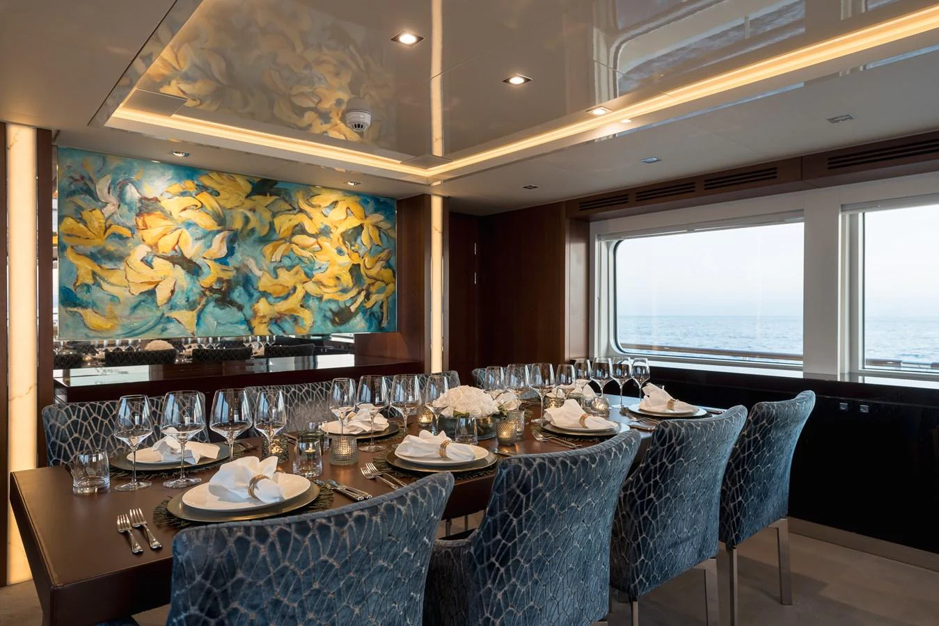 The yacht's dining area features an elegant table setting with a vibrant wall mural and large windows offering sea views. aboard ORIZZONTE Yacht for Sale