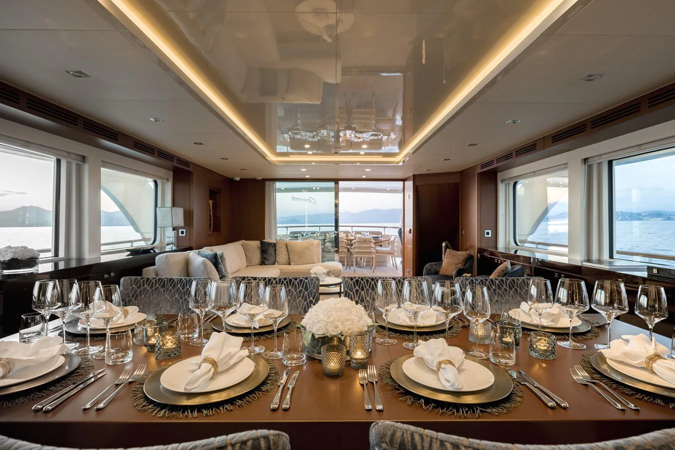 The yacht's dining area features an elegantly set table with a view of the sea through large windows. aboard ORIZZONTE Yacht for Sale