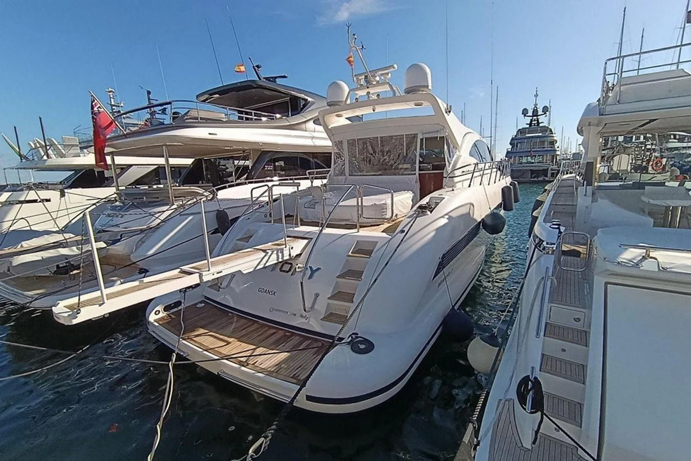 The yacht is docked at a marina, showcasing its sleek aft deck and inviting outdoor space. aboard MANGUSTA 72 Yacht for Sale