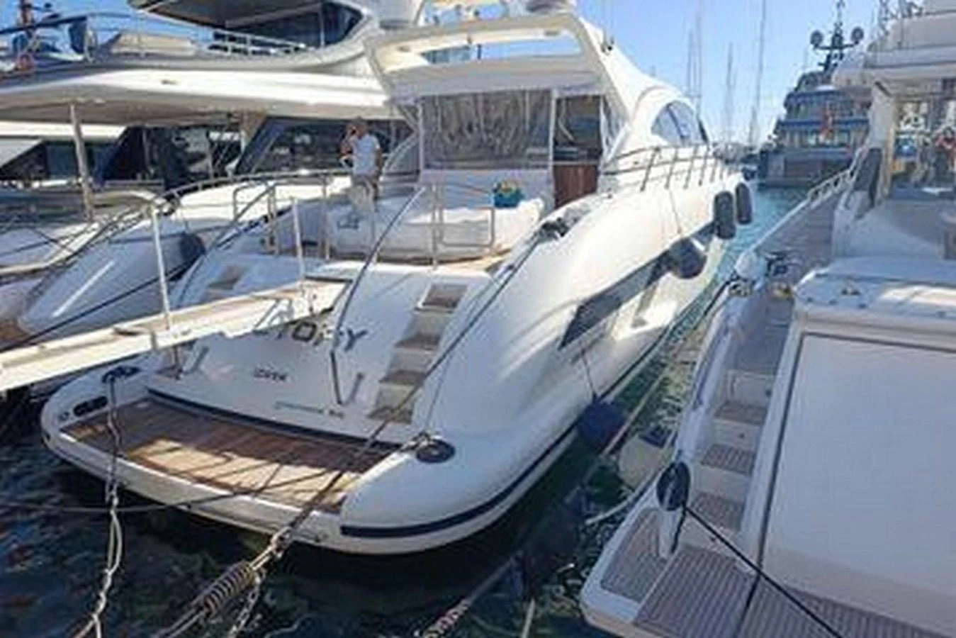 The yacht is docked at a marina, showcasing its sleek aft deck and inviting swim platform. aboard MANGUSTA 72 Yacht for Sale