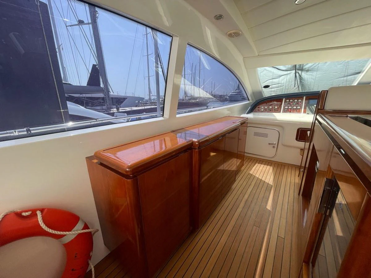 The yacht's helm area features polished wood cabinetry and a sleek control panel, with large windows offering a view of the marina. aboard MANGUSTA 72 Yacht for Sale