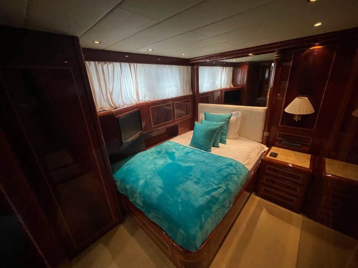 The stateroom features a cozy bed with vibrant blue accents and elegant wooden cabinetry. aboard MANGUSTA 72 Yacht for Sale