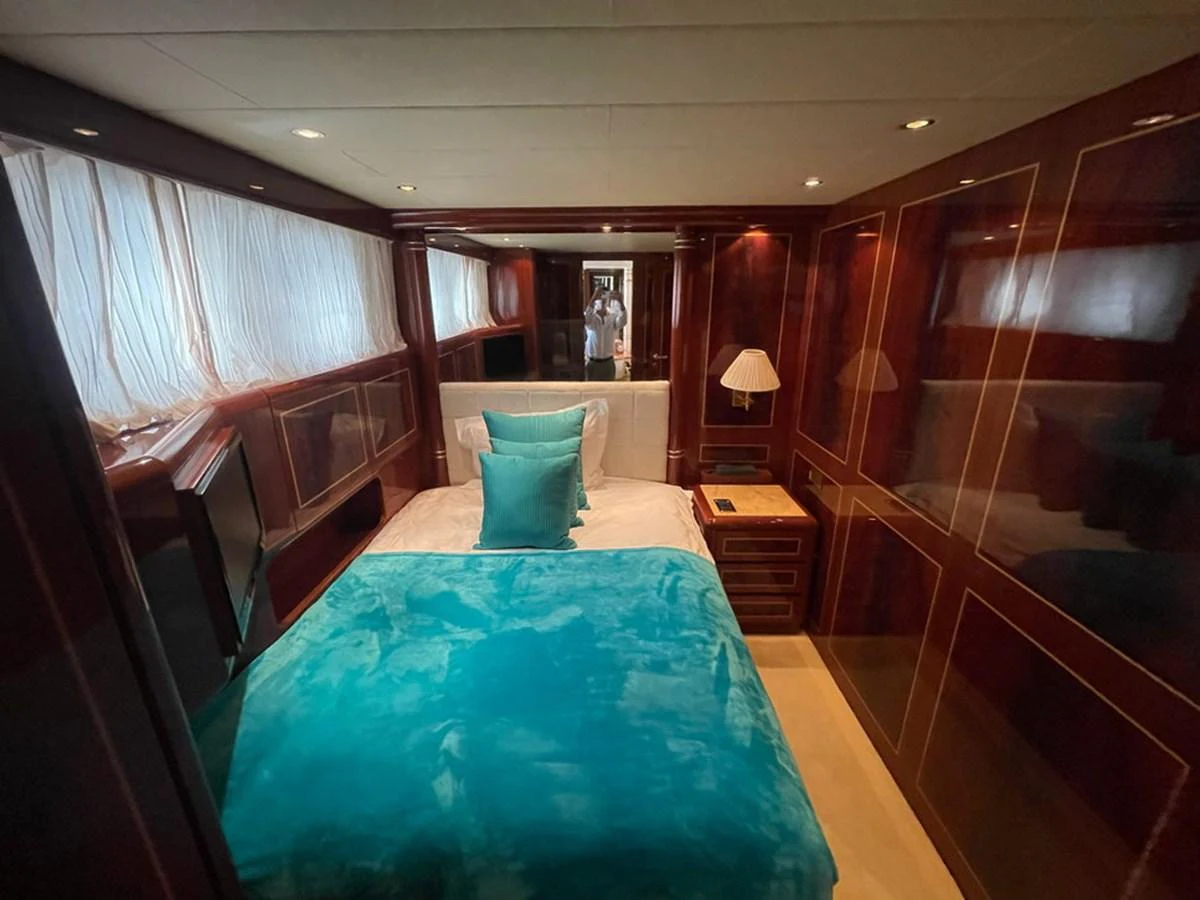 A cozy stateroom with rich wood paneling and a plush bed adorned with teal accents. aboard MANGUSTA 72 Yacht for Sale