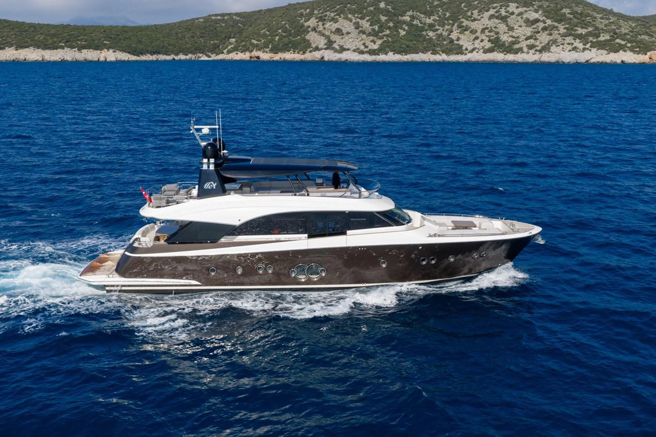 A sleek yacht cruises through vibrant blue waters with a scenic coastline in the background. aboard BELLA LUNA Yacht for Sale