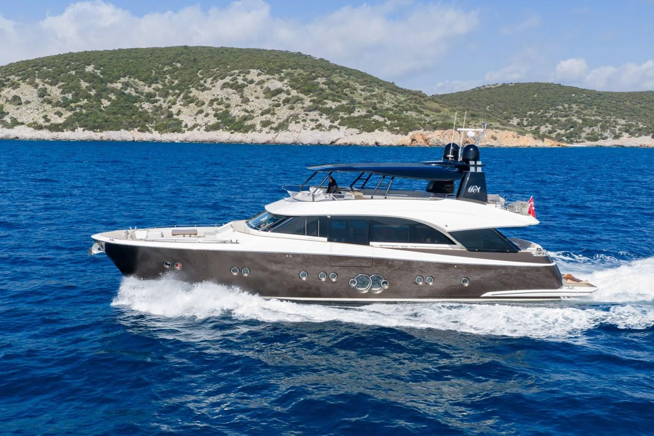 A sleek yacht cruises through clear blue waters with a scenic coastline in the background. aboard BELLA LUNA Yacht for Sale