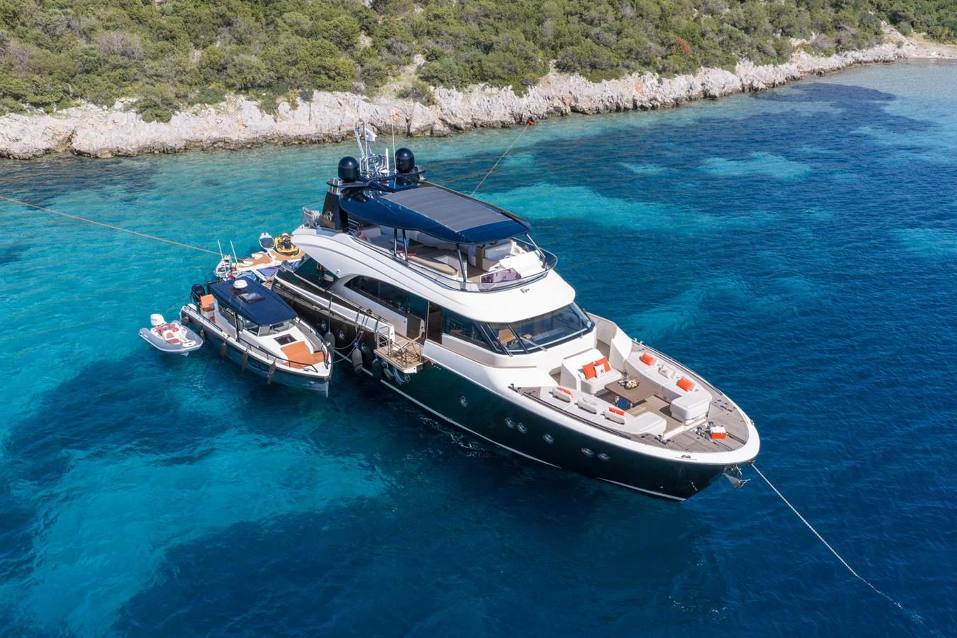 A luxurious yacht anchored in a serene bay with clear blue waters and lush greenery in the background. aboard BELLA LUNA Yacht for Sale
